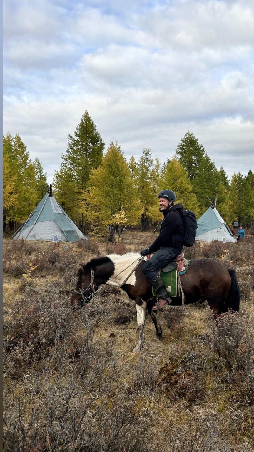 A rider on horseback beside two tents in open grassland.