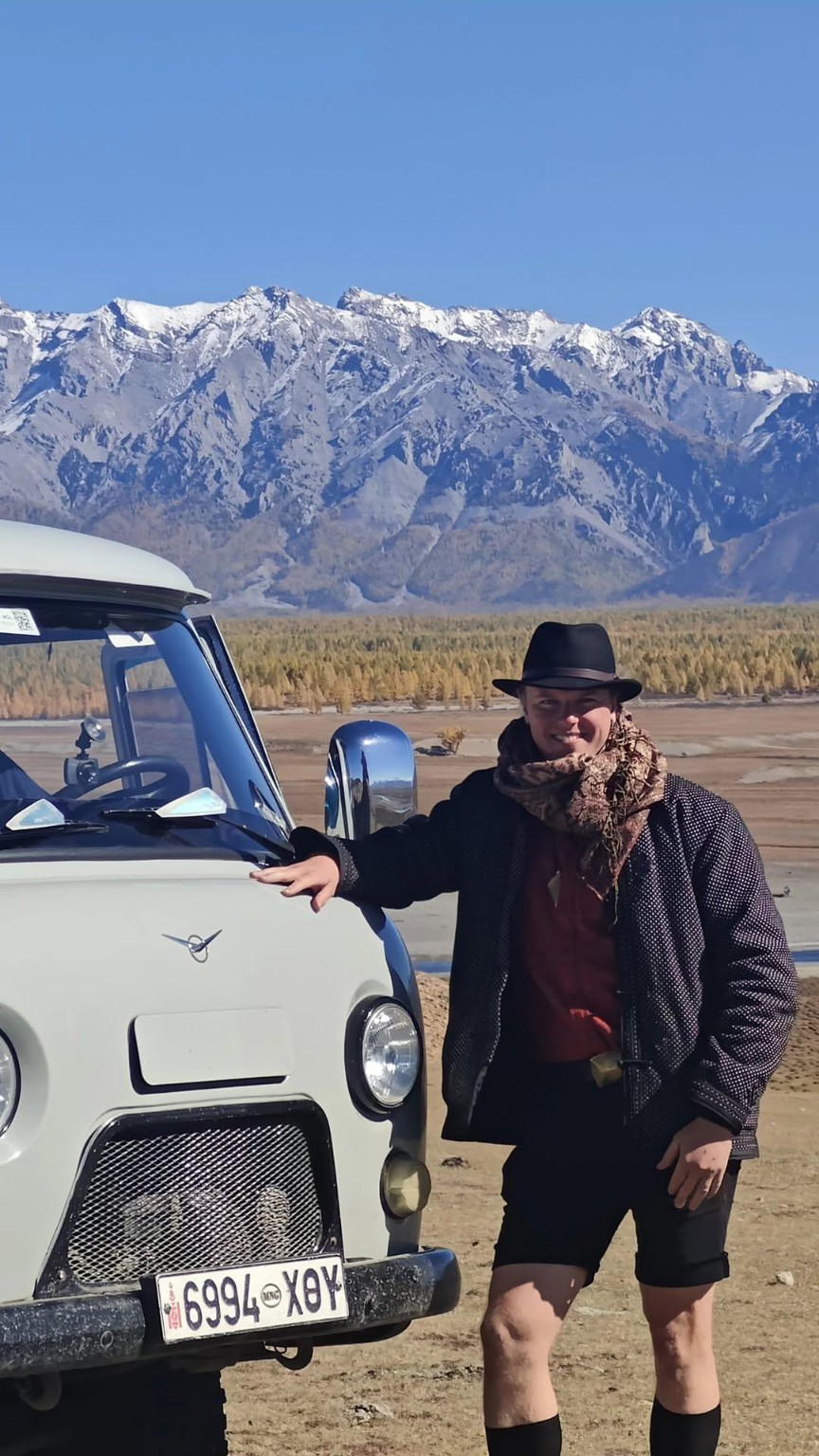 A person beside a pale van with a snow-topped mountain range behind.