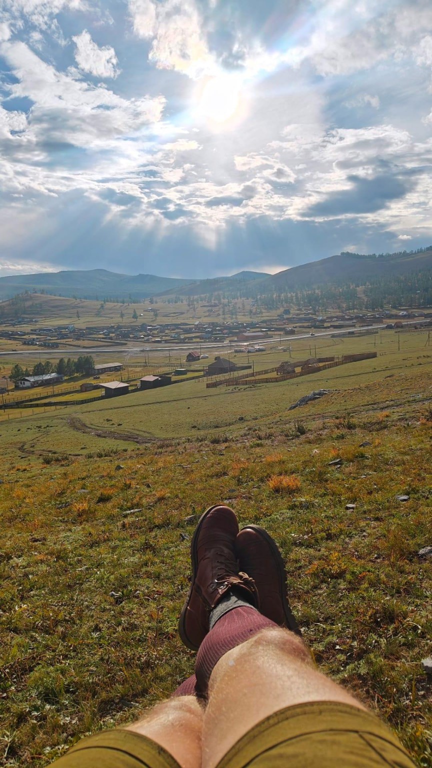 Booted feet resting above a broad valley beneath broken sunlight.